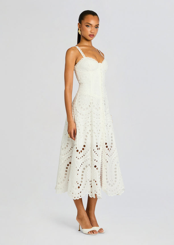 Model wearing ivory Solace Long Dress with intricate eyelet embroidery and scalloped hem, paired with white heels.