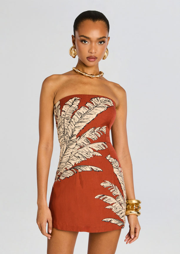 Three quarter front view of a model wearing the rust palm leaf strapless mini dress with gold jewelry.