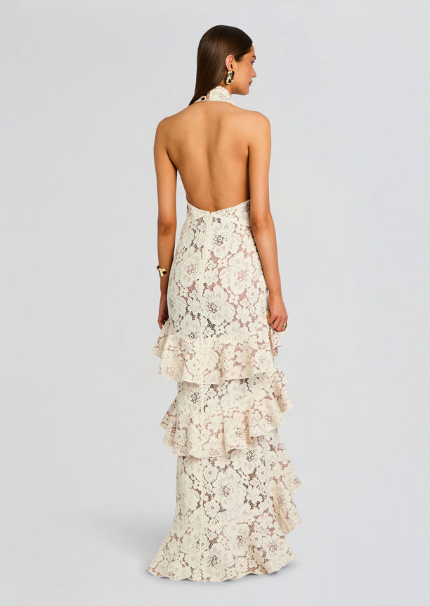 Back view of ivory lace Senara dress with an open halter back and a tiered ruffle skirt tied by a black bow at the waist.