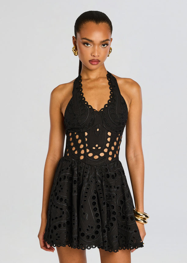 Model wearing a black Sandlight Short Dress with circular cutouts and a halter neckline.