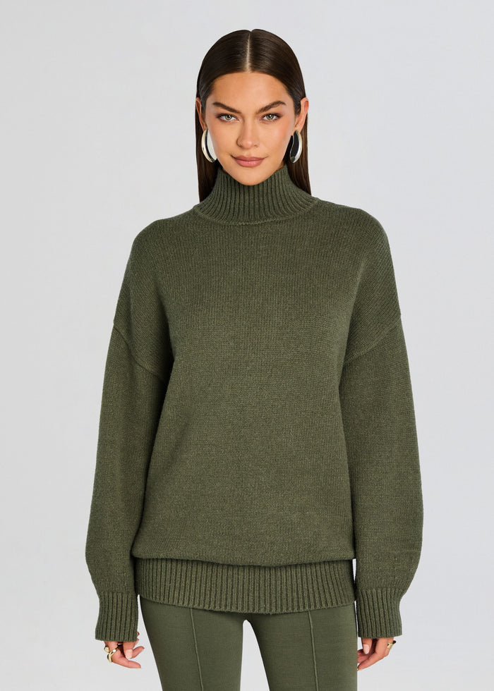Woman wearing an olive green chunky turtleneck sweater with a relaxed fit. media 1 of 5