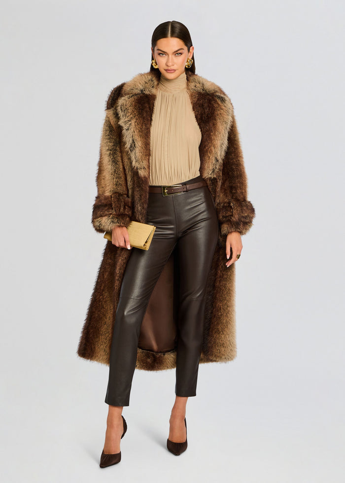 Model wearing a brown fur coat over a beige top with Cyra Leather Leggings and a beige clutch. media 2 of 5