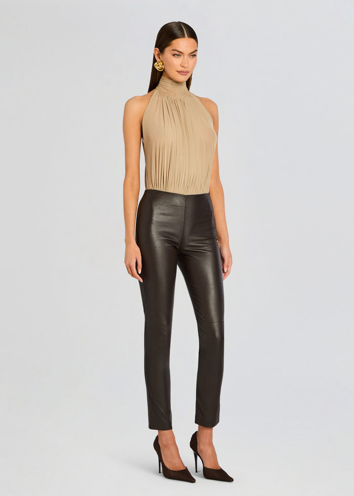 Full-length view of a model in a beige pleated halter top paired with Cyra Leather Legging and brown heels. media 4 of 5