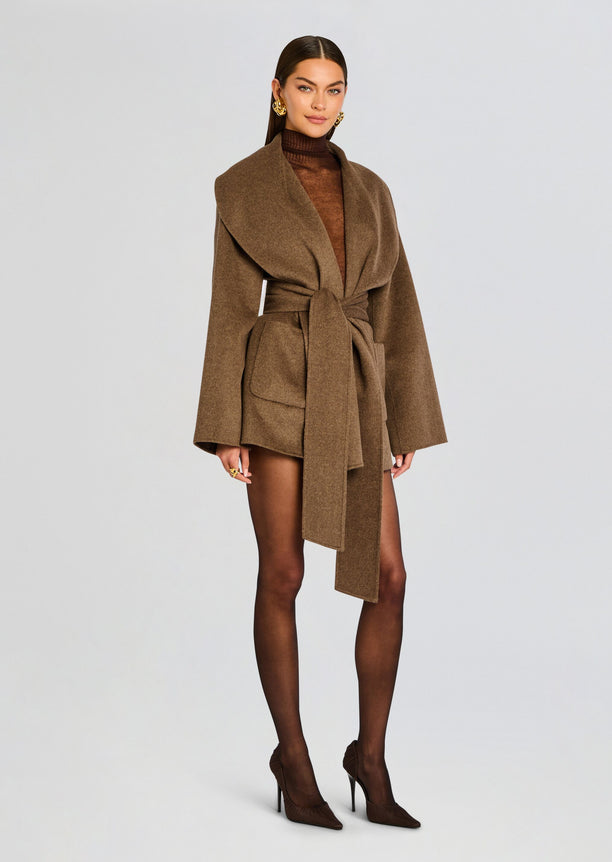 Full-body shot of a model wearing a brown Dulcetta wool coat belted at the waist, paired with sheer black tights and brown heels.