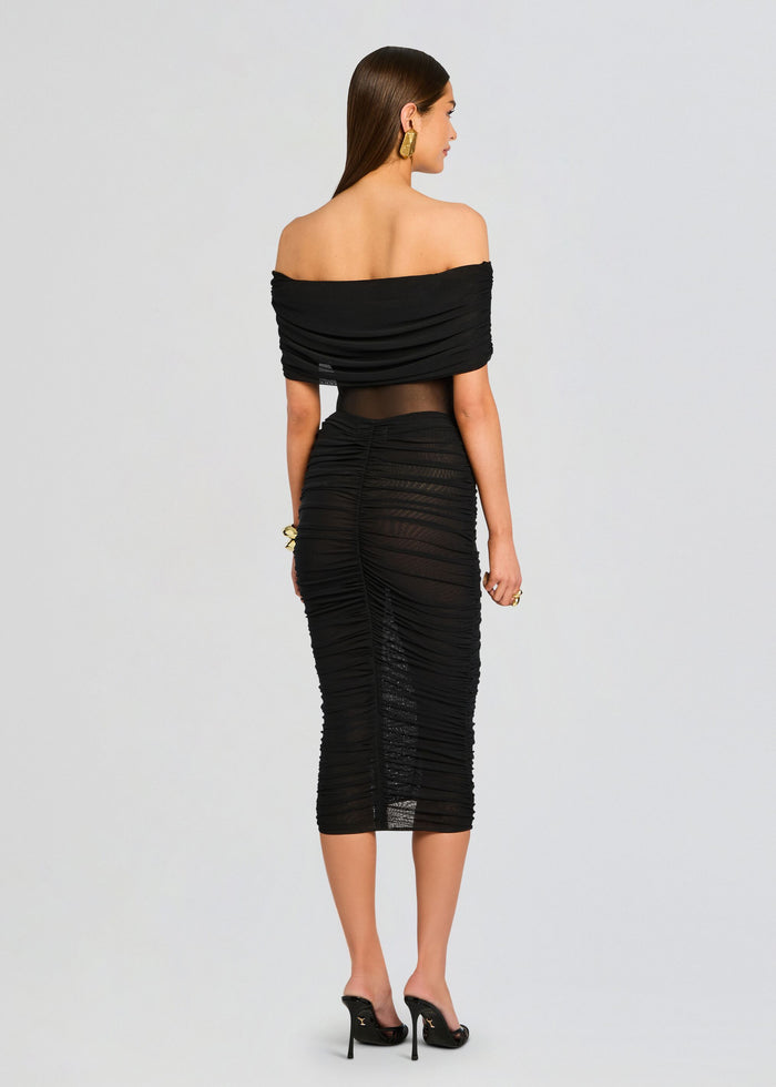 Back view of a model in a black off the shoulder ruched mesh midi skirt with a sheer midsection media 5 of 5
