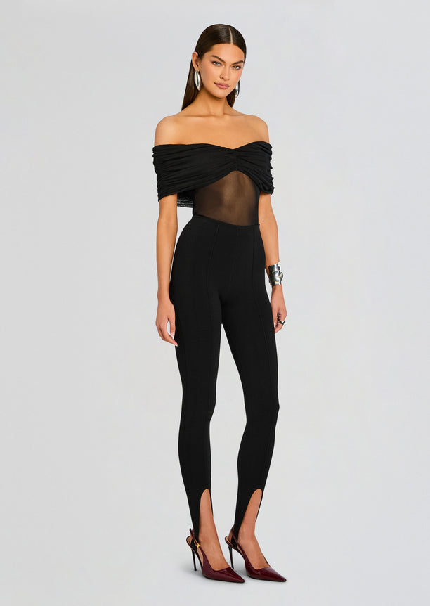 Front view of a model wearing black Kelsey Stirrup Leggings with an off the shoulder ruched top and burgundy heels.