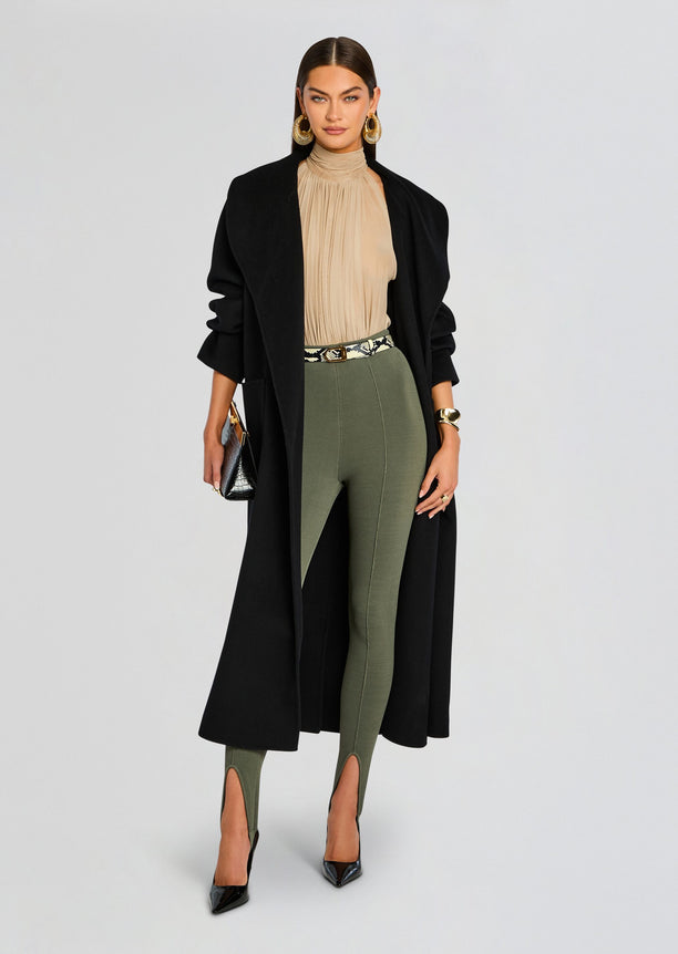 Model wearing Kelsey Stirrup Legging in olive green with a beige pleated high neck top and a long black coat