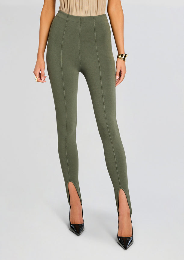 Model in olive Kelsey Stirrup Leggings with vertical seam panels and front ankle slits, paired with pointed heels.