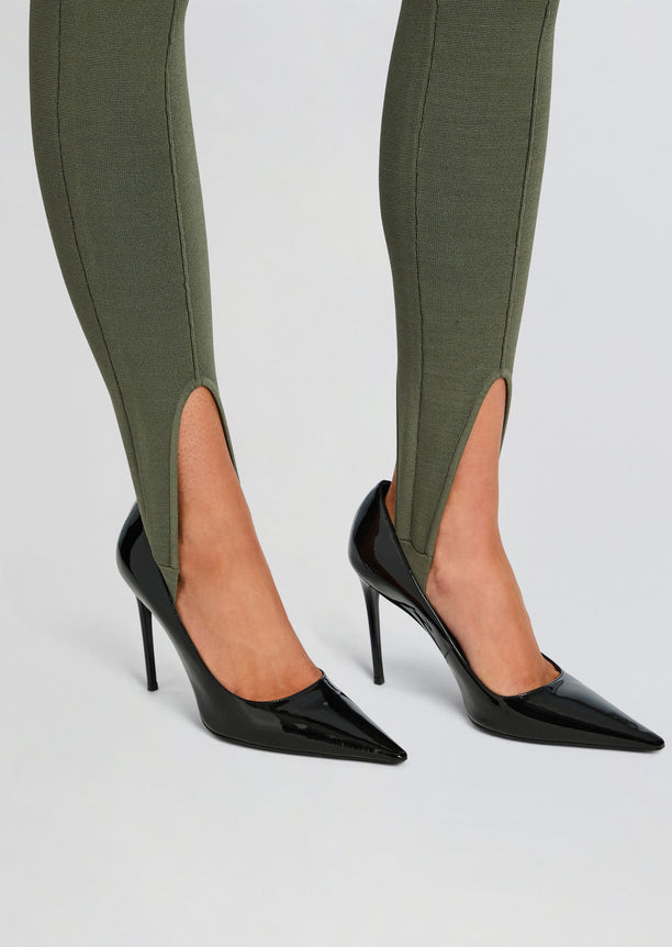 Close-up of olive green stirrup leggings with ankle slits and black patent stilettos