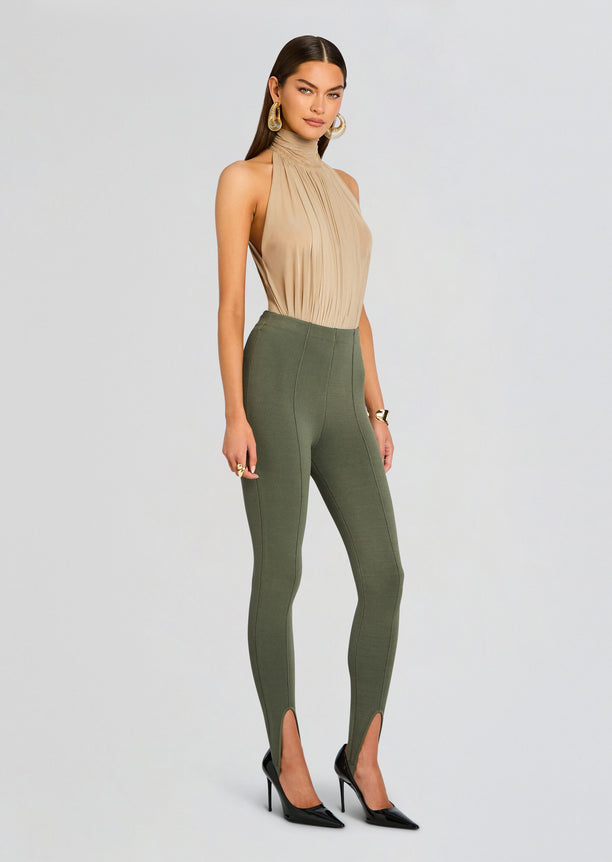 Full body shot of a model in a beige pleated halter top with olive green stirrup leggings and black heels