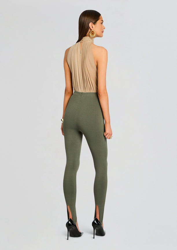 Back view of a model wearing a beige halter top and olive green stirrup leggings with ankle slits