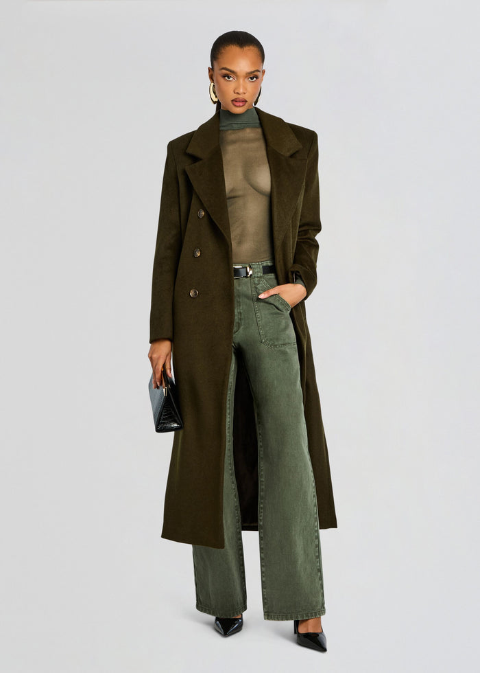 Model wearing a long olive wool coat over a sheer olive-green top and olive-green wide-leg pants, with black heels and a small black clutch. media 6 of 6