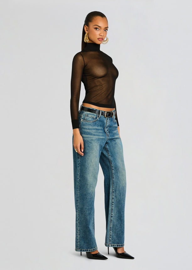 Full-length shot of a model in the Lainey Top a sheer black turtleneck paired with blue jeans and a black belt