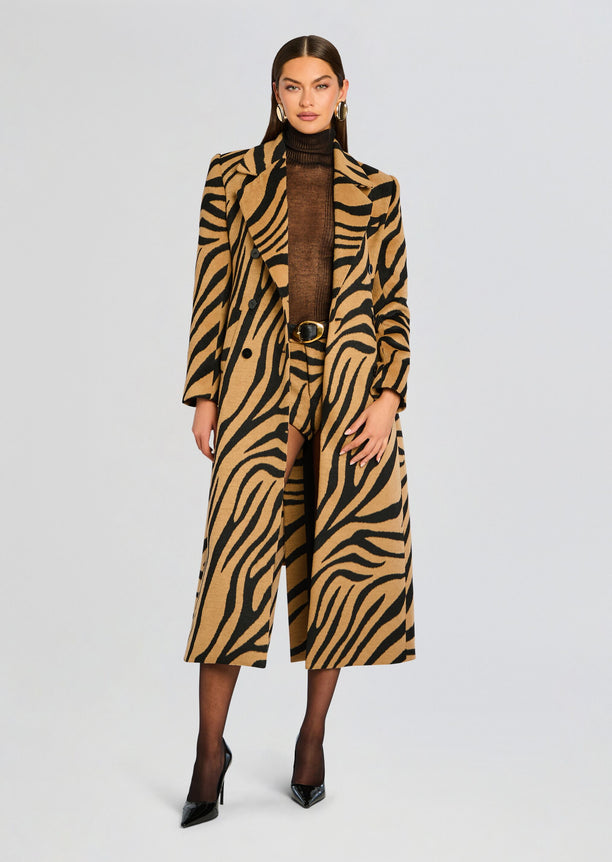 Model wearing a camel and black tiger stripe Petal Coat over a brown top with a belt and black heels.