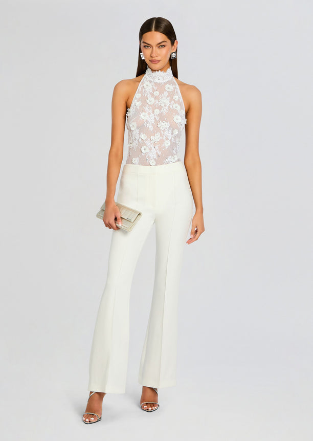 Model wearing Saga Lace Embellished Bodysuit with a high neck and floral lace detailing paired with white tailored trousers.