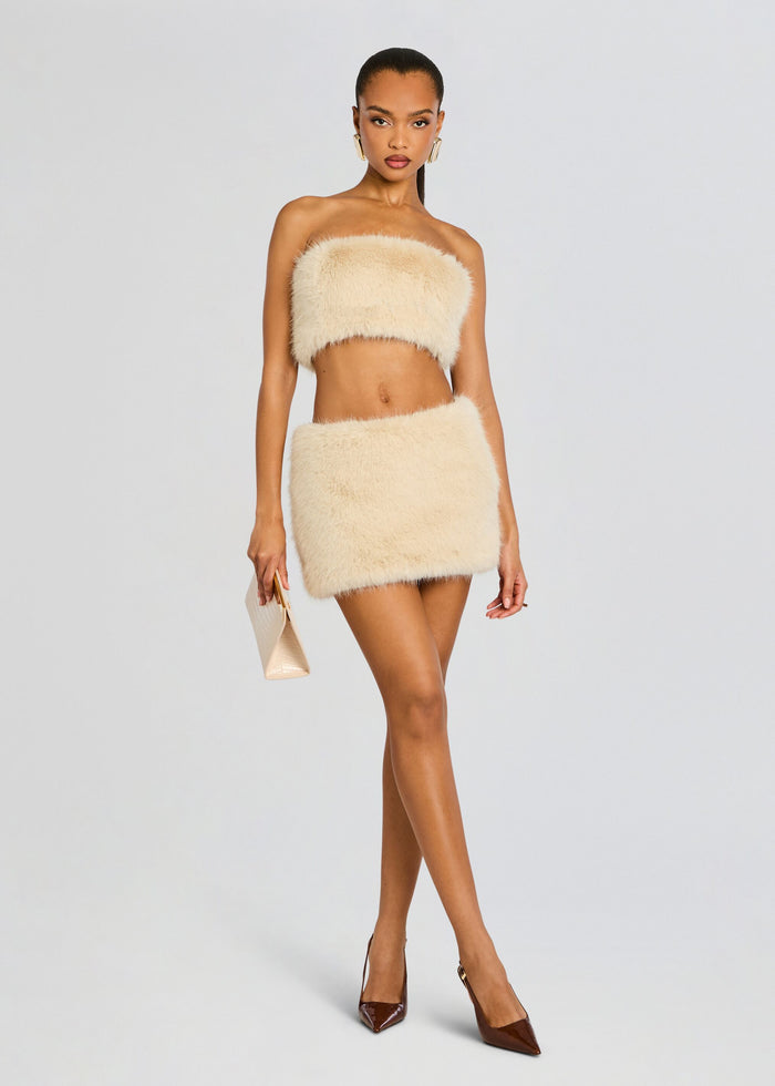 Model in beige faux fur bandeau and matching mini skirt poses with a beige clutch and brown pointed heels media 6 of 7