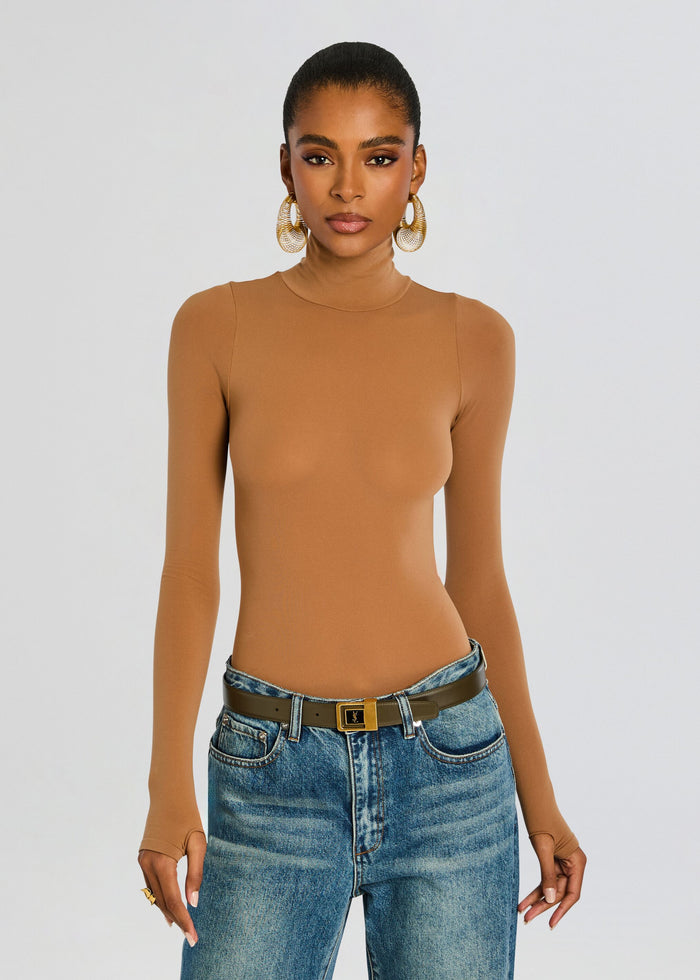 Model in camel ballet turtleneck bodysuit with blue jeans and a dark brown belt, gold hoop earrings. media 1 of 6