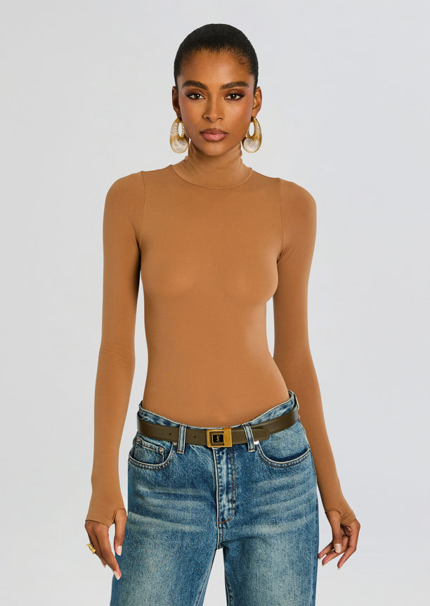 Model in camel ballet turtleneck bodysuit with blue jeans and a dark brown belt, gold hoop earrings.