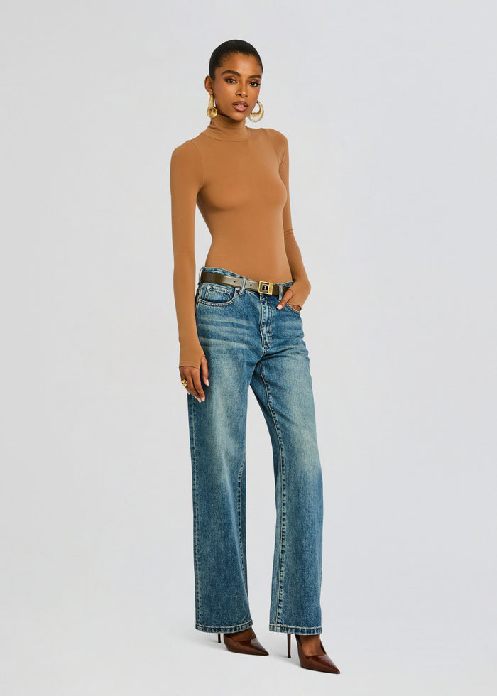 Model in tan Ballet Turtleneck Bodysuit with blue jeans and a belt, accessorized with large gold hoop earrings media 4 of 6