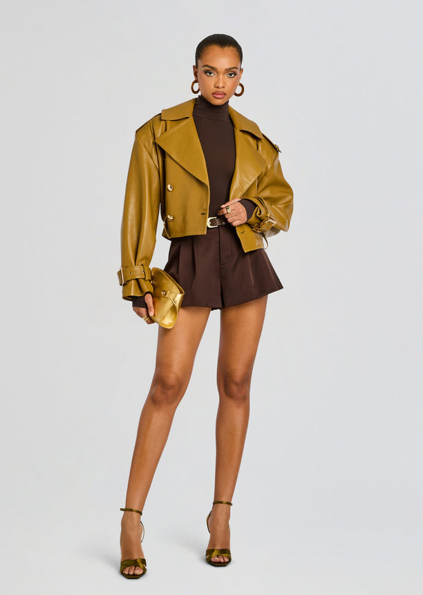 Model wearing a tan cropped leather jacket over a dark brown turtleneck bodysuit and matching high waisted brown shorts.