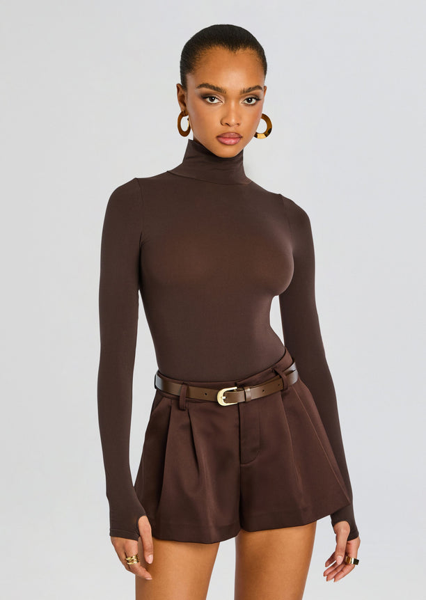 Model in Ballet Turtleneck Bodysuit with brown high-waisted shorts belt and large gold hoop earrings.