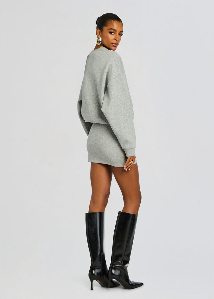 Side profile of a model in the gray Dionne Mini Dress showing an oversized top and fitted mini skirt with tall black boots media 4 of 5