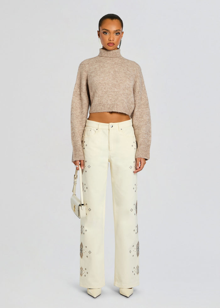 Full body shot of a model in a cropped beige knit sweater and cream embroidered jeans with geometric patterns. media 2 of 6