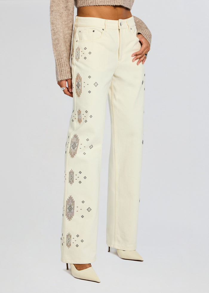 Cream Embroidered Jean with brown geometric motifs down the legs and a beige knit top. media 1 of 6