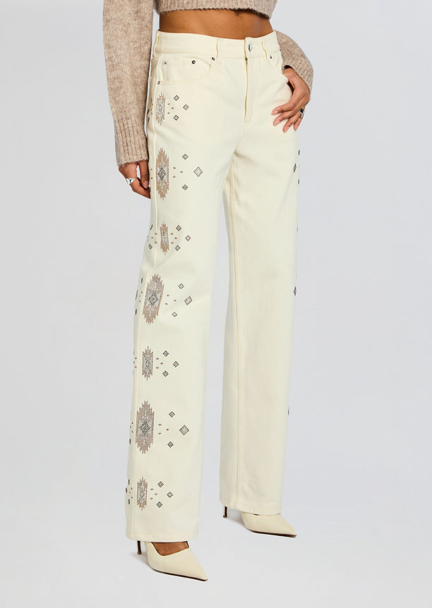 Cream Embroidered Jean with brown geometric motifs down the legs and a beige knit top.
