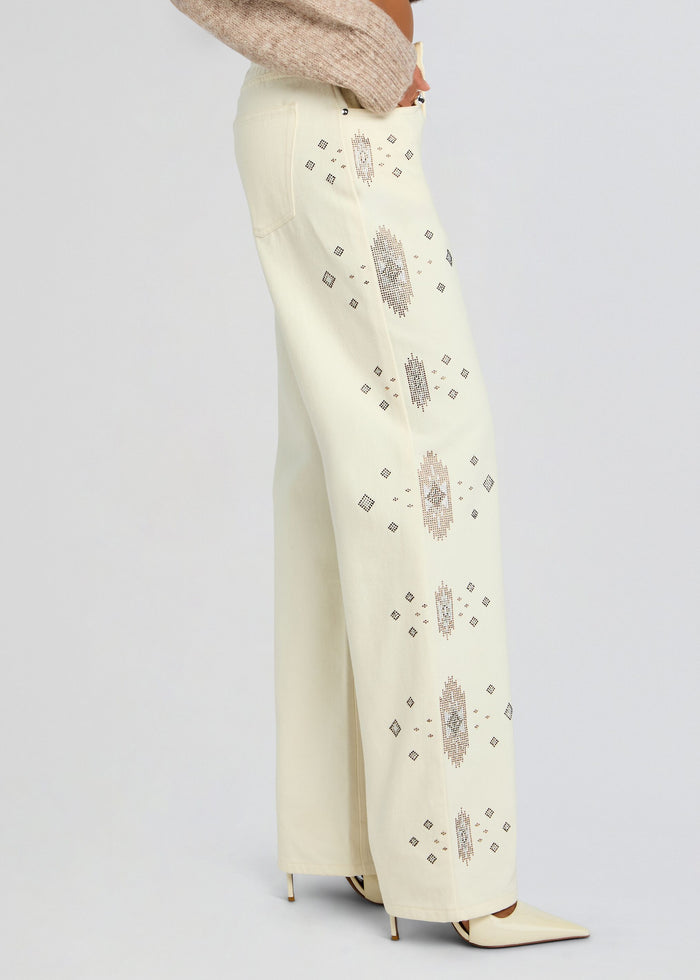 Side view of cream embroidered jeans with vertical diamond motifs and scattered geometric embroidery along the leg. media 4 of 6