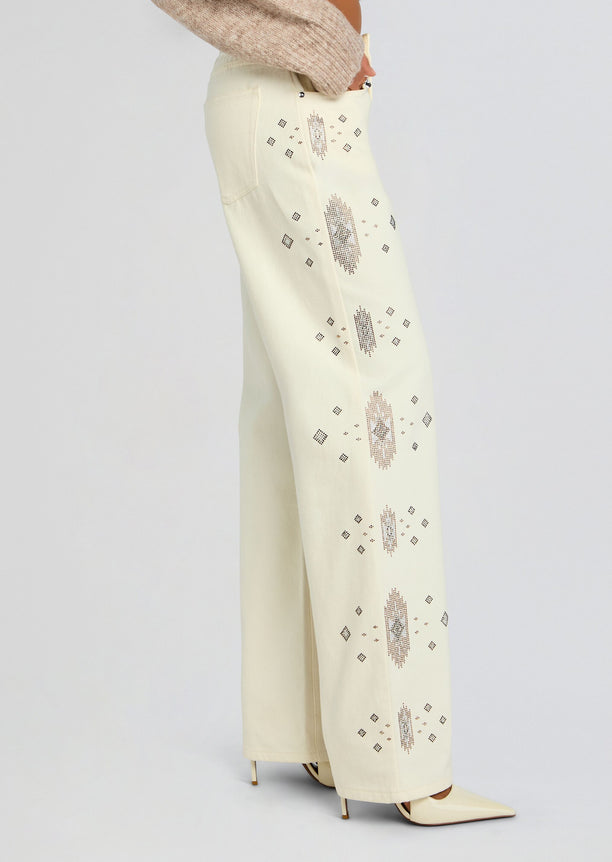 Side view of cream embroidered jeans with vertical diamond motifs and scattered geometric embroidery along the leg.