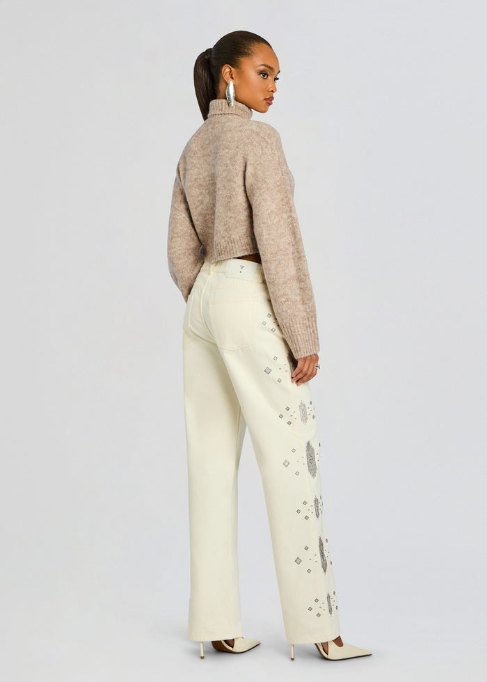 Back view of a model wearing a beige cropped knit sweater and pale cream jeans with silver diamond embroidery along the legs. media 5 of 6