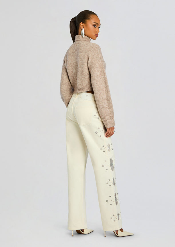 Back view of a model wearing a beige cropped knit sweater and pale cream jeans with silver diamond embroidery along the legs.