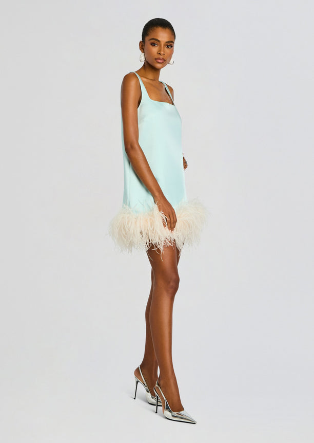Full-length side view of a model wearing a light mint Ragna Feather Dress with a feathered hem and metallic silver heels.