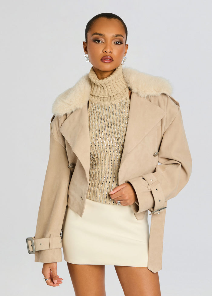 Front view of a model in a tan Rubee Coat with a plush fur collar over a beaded sweater and cream mini skirt. media 1 of 6