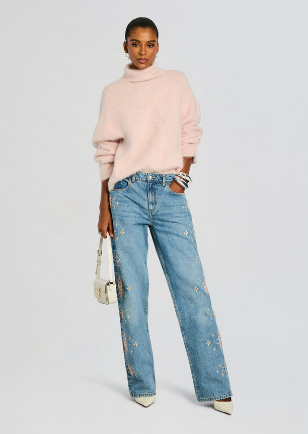 Model wearing a pink fuzzy turtleneck and light wash Vero Embroidered Jean with scattered embroidery and a white handbag.