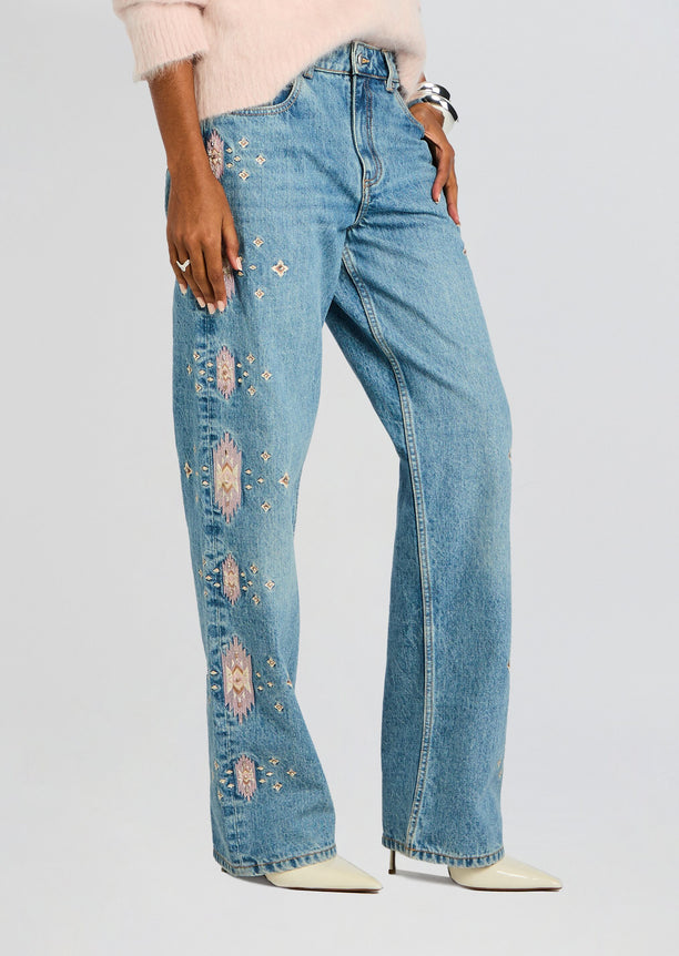 Full length Vero Embroidered Jean with pink embroidery down the left leg, styled with a soft pink sweater and cream pointed boots.