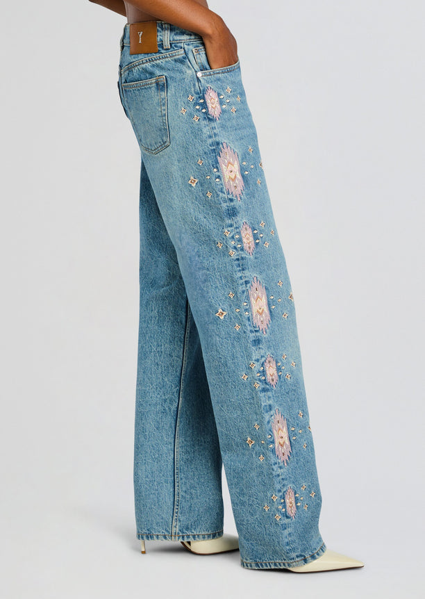 Side view of light wash Vero Embroidered Jean with pink diamond embroidery along the leg and a leather patch at the waistband.
