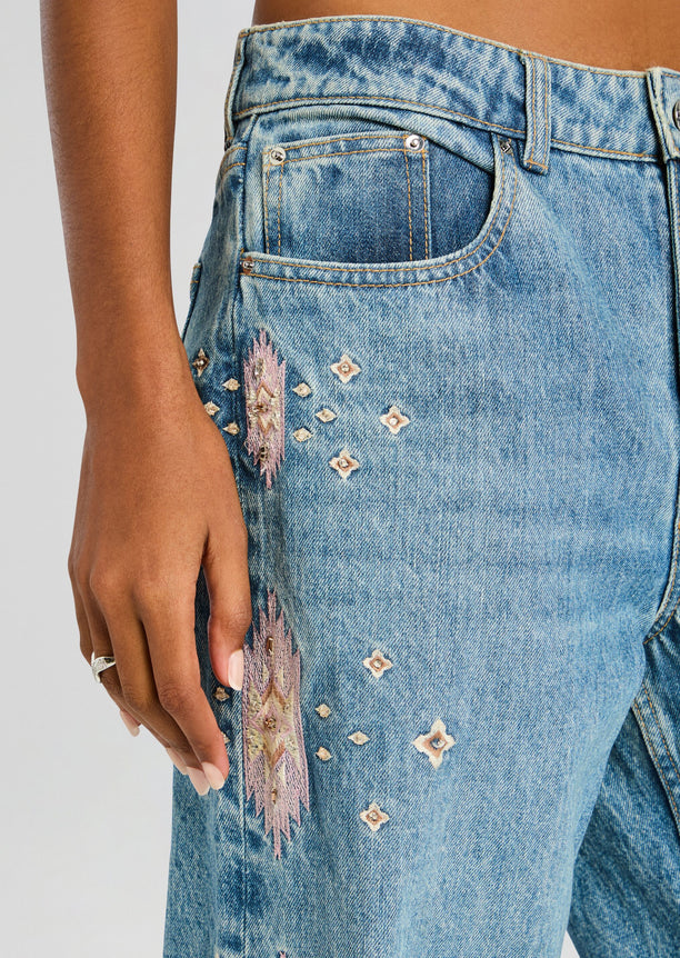 Close-up of Vero Embroidered Jean front pocket and side panel with pink embroidery on blue denim.