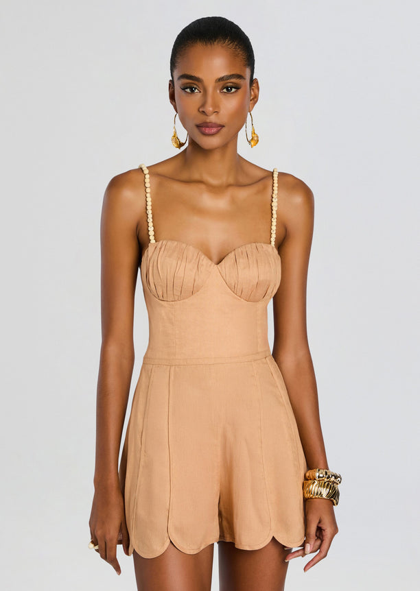 Model wearing a coral romper with beaded shoulder straps and scalloped hem shorts.