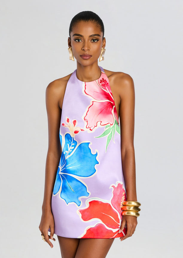 Model wearing a halter neck dress with large tropical florals in pink red and blue on a lavender background.