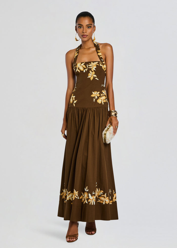 Full-length model wearing a brown halter maxi dress with yellow floral embroidery and a floral hem border. media 1 of 5