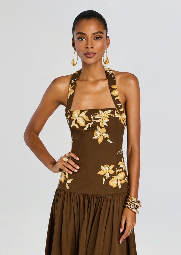 Front view of brown halter maxi dress with yellow floral embroidery on the bodice and a flowing skirt.