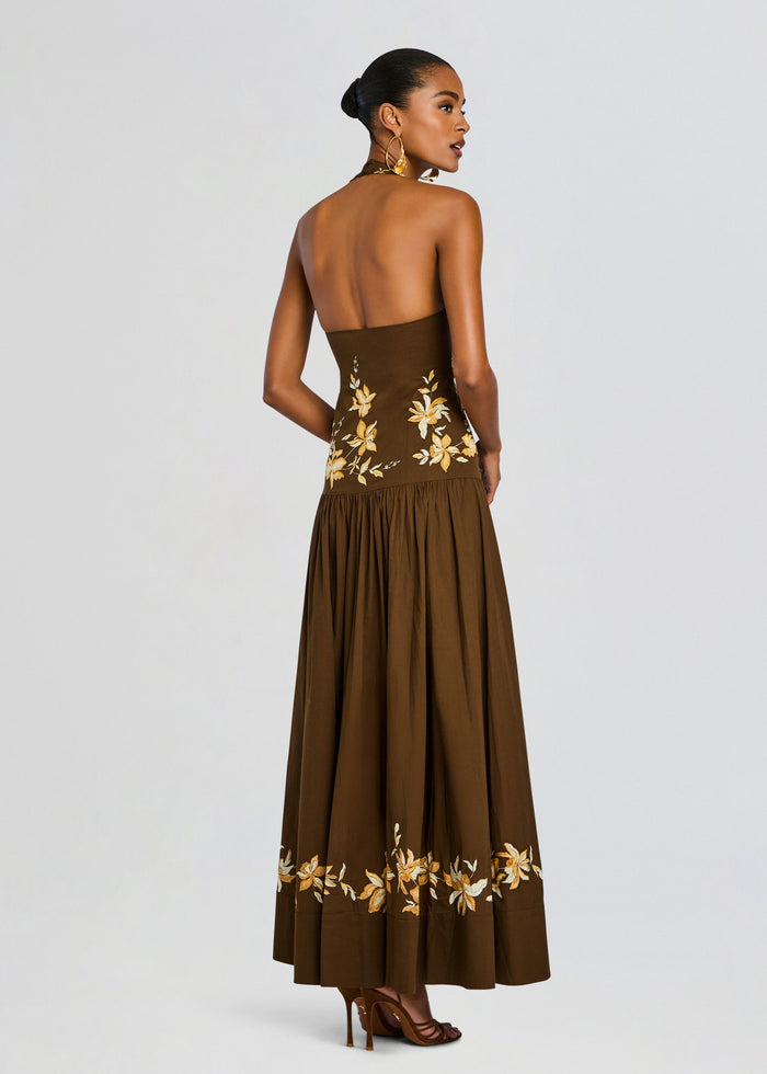 Back view of a brown halter maxi dress with yellow floral embroidery on the bodice and hem, model wearing gold heels. media 4 of 5