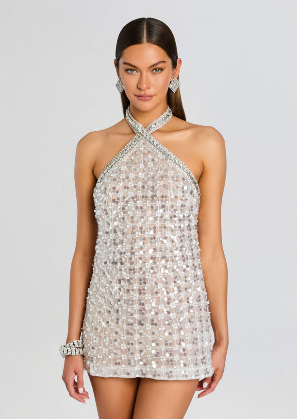 Front view of a silver embroidered halter dress with a crisscross neckline and shimmering grid pattern, model wearing statement earrings.