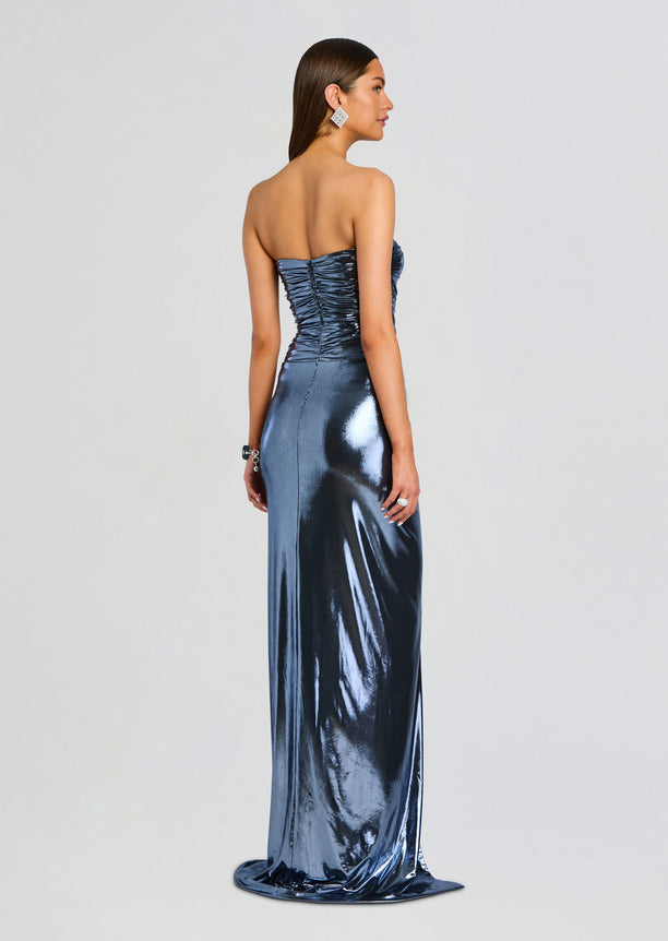 Back view of the Maytal Dress on a model strapless metallic blue gown with ruched back and floor length drape