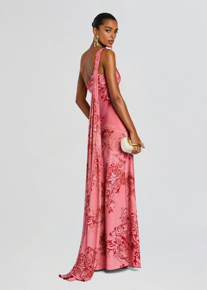 Side view of pink floral Vine One Shoulder Sash Dress with a long draped sash down the back, model holding a small white clutch. media 1 of 5