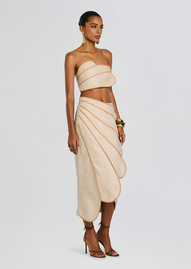 Beige bandeau crop top with peach piping paired with a matching wrap skirt featuring curved layered panels.