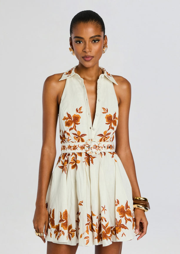 Model wearing a cream sleeveless Ayra dress with orange floral embroidery and a round belt buckle.