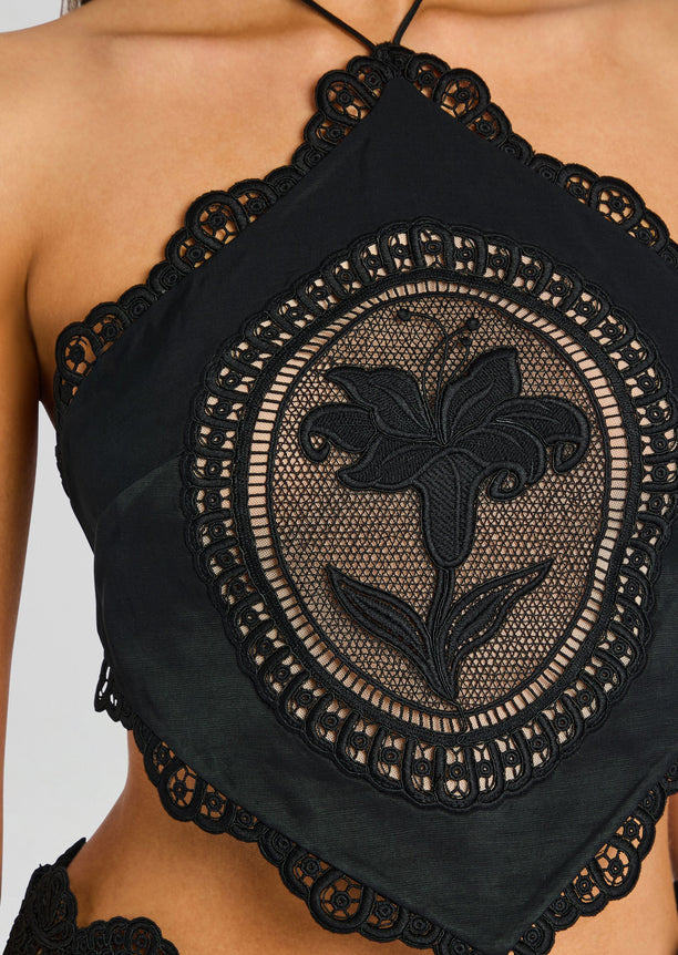 Close up of the black lace halter top showing a circular embroidered flower panel and scalloped trim